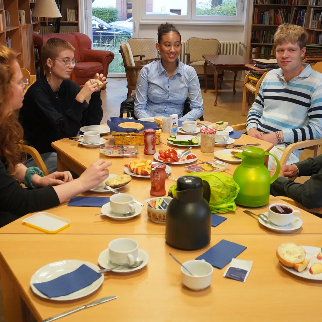 Mehrere Menschen sitzen im Kreis an einem Tisch, reden und essen.