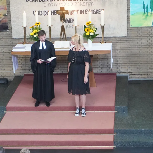 Am Altar stehen der Pfarrer, Herr Bismarck, und die neue Gemeindesekretärin, Frau Freimuth